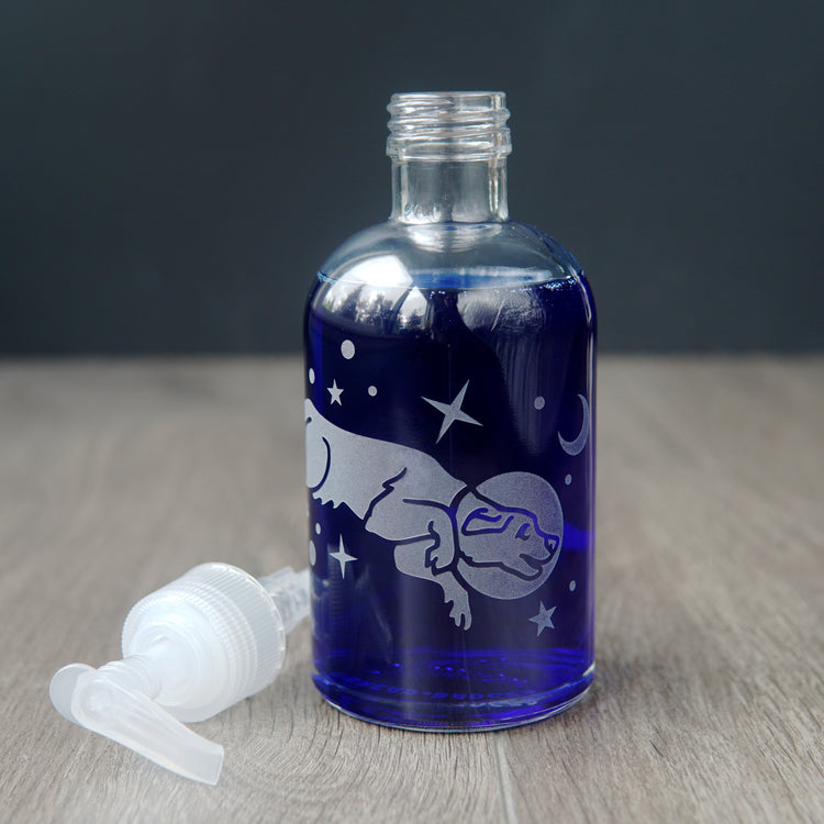 space dog soap dispenser filled with dark blue dish soap. the pump top is laying on the table next to the bottle.