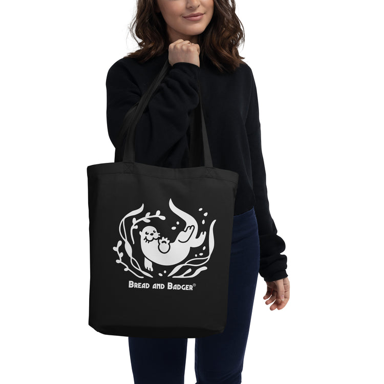 Person holding a black tote bag with a white otter and 'Bread and Badger' text on a white background