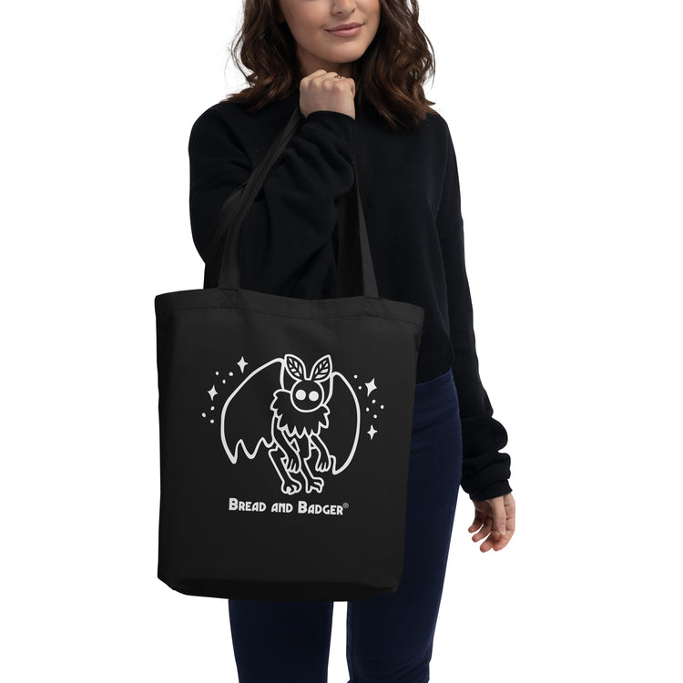 Person holding a black tote bag with a white mothman  graphic and 'Bread and Badger' text on a white background