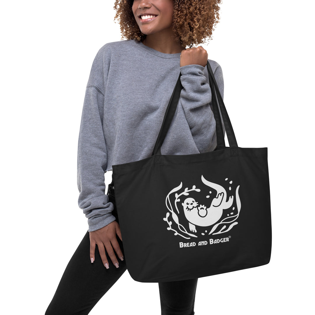 Person holding a black tote bag with a white otter and 'Bread and Badger' text on a white background
