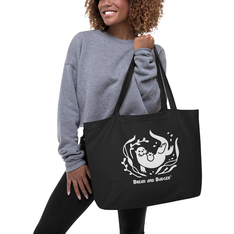 Person holding a black tote bag with a white otter and 'Bread and Badger' text on a white background