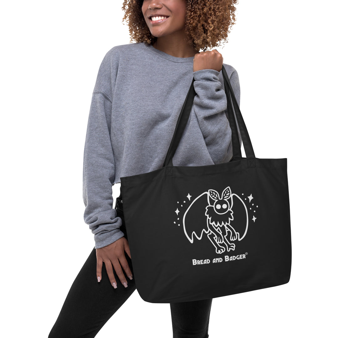 person holding a black tote bag with a white mothman  graphic and 'Bread and Badger' text on a white background
