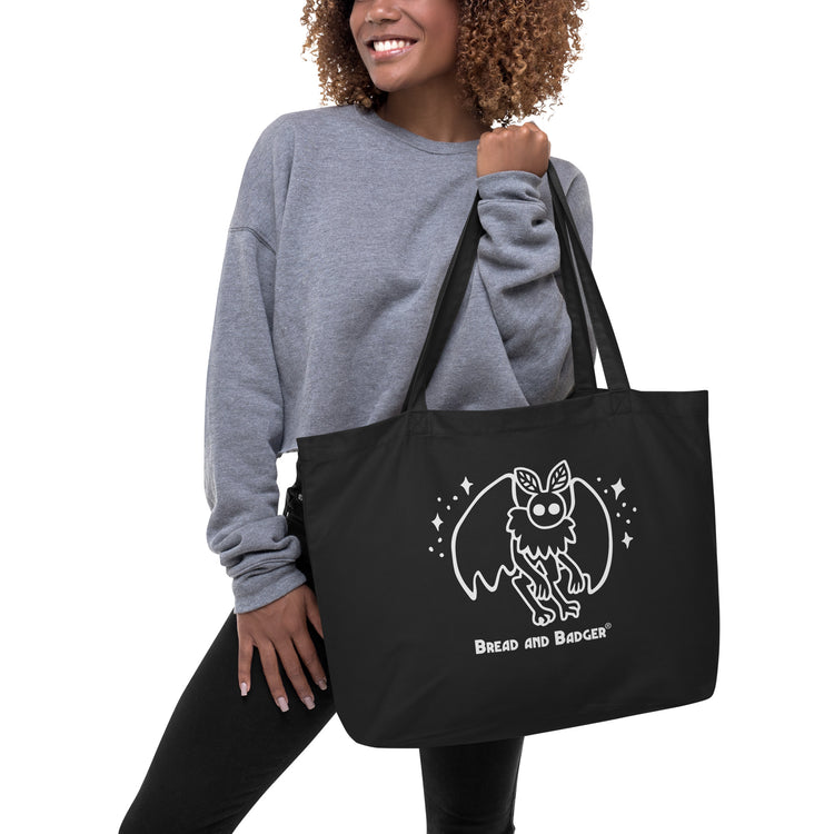 person holding a black tote bag with a white mothman  graphic and 'Bread and Badger' text on a white background