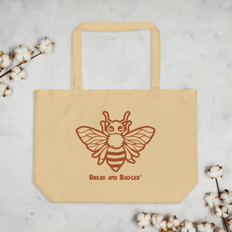 Beige tote bag with a bee design and 'Bread and Badger' text on a light gray background with cotton branches.