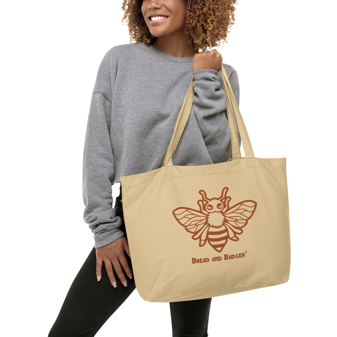 Woman holding a beige tote bag with a bee design and 'Bread and Badger' text.