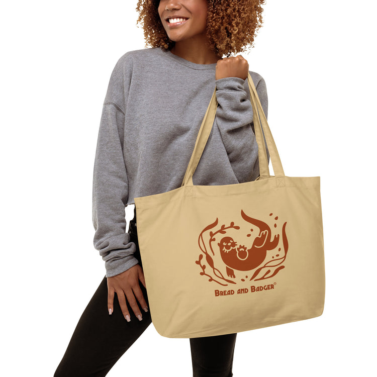 Woman holding a beige tote bag with brown otter and 'Bread and Badger' text on a white background