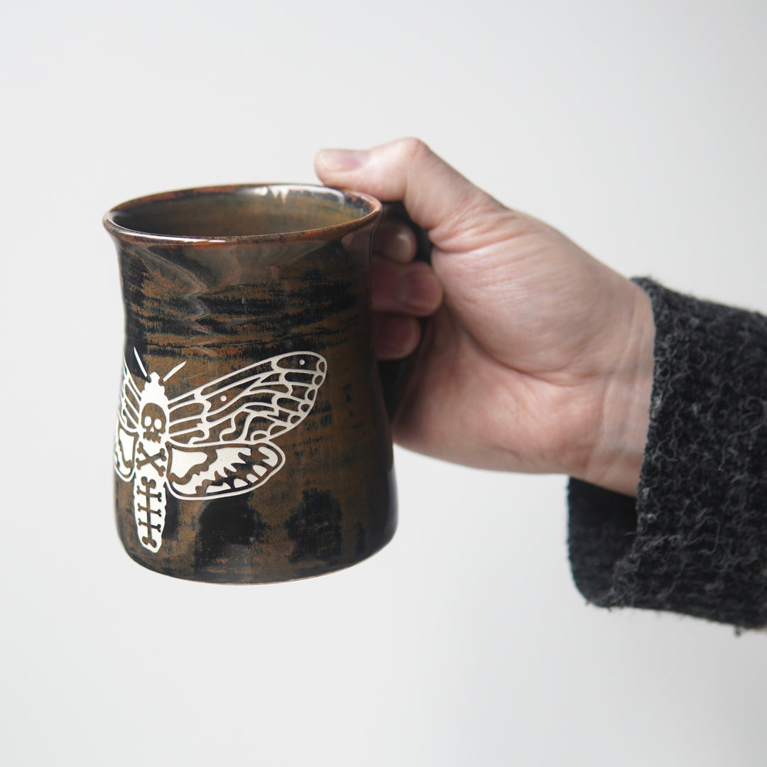 brown deaths head hawkmoth pottery mug, held by a hand