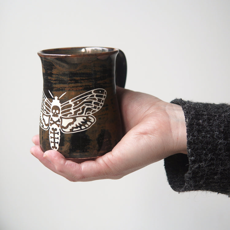 brown deaths head hawkmoth pottery mug, held in the palm of a hand