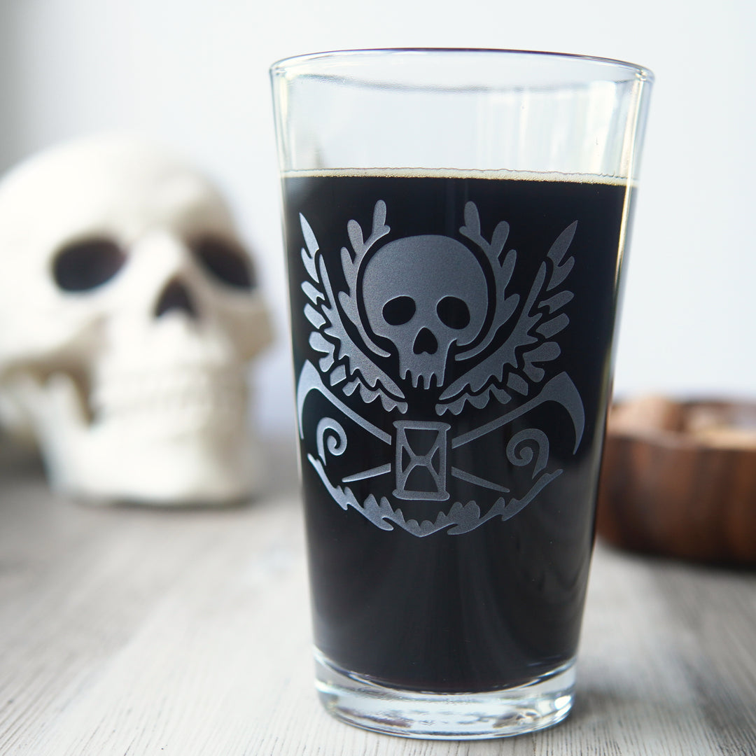 pint glass engraved with a winged skull, scythes, and hourglass