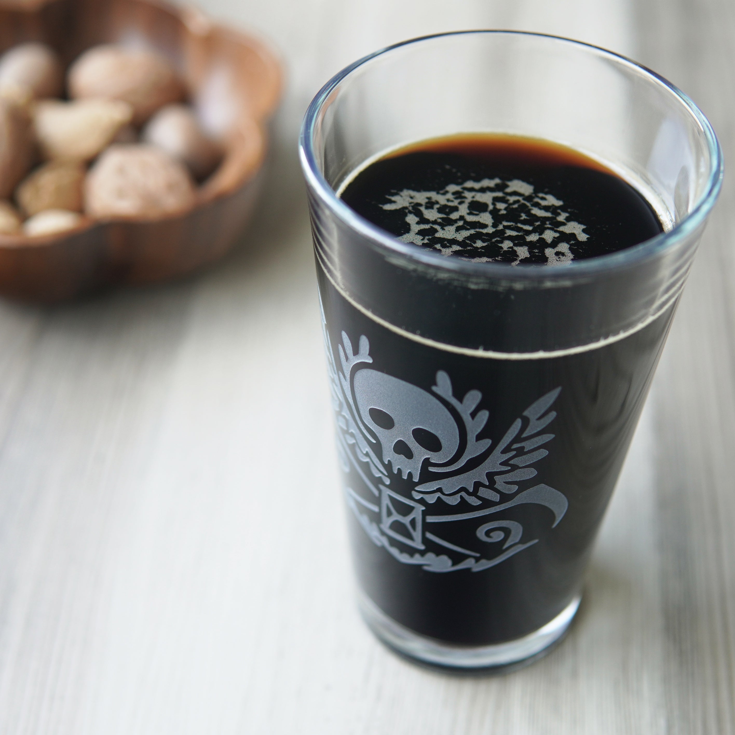 pint glass full of dark beer, engraved with a winged skull, scythes, and hourglass