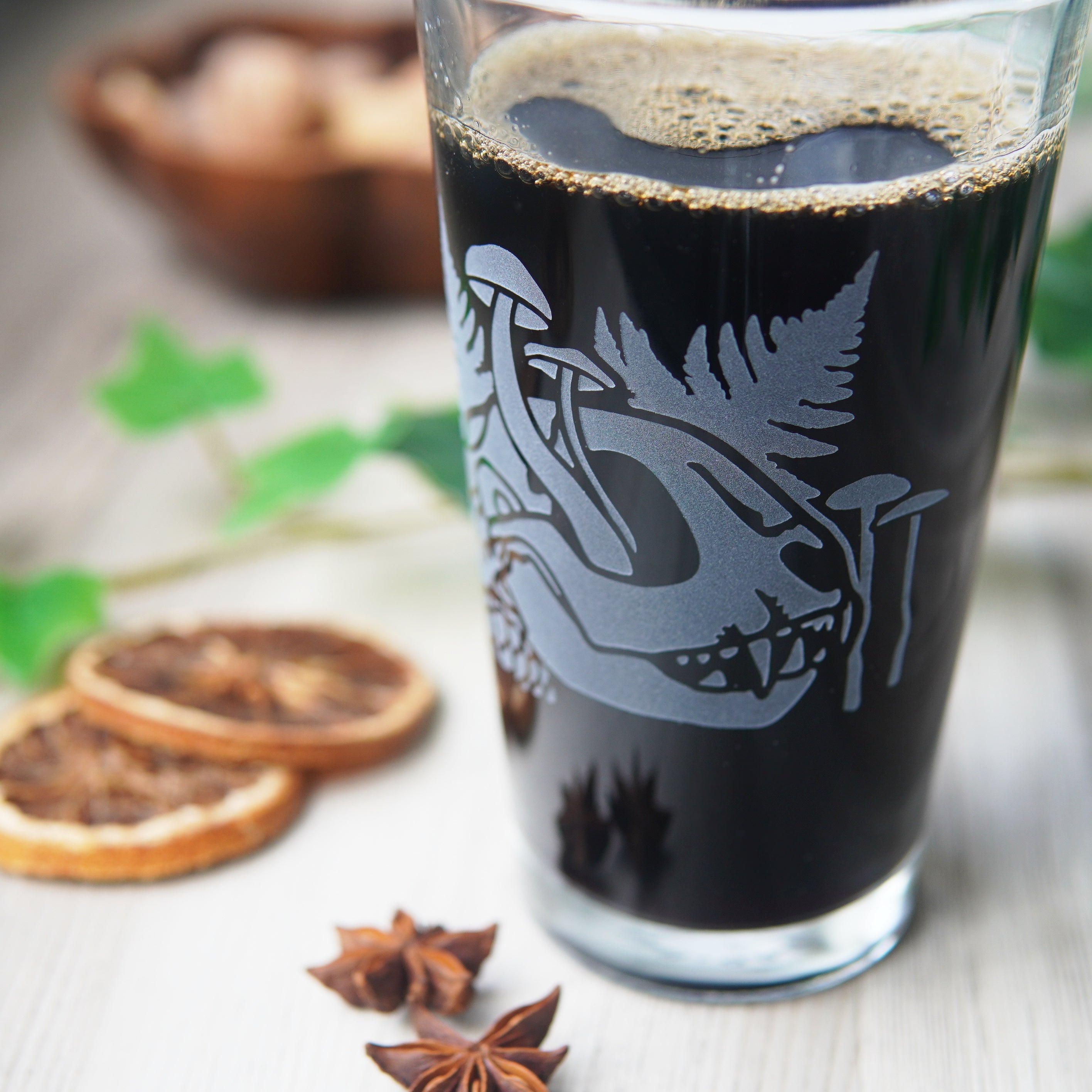 pint glass full of beer engraved with a cat skull, ferns, and mushrooms growing through it