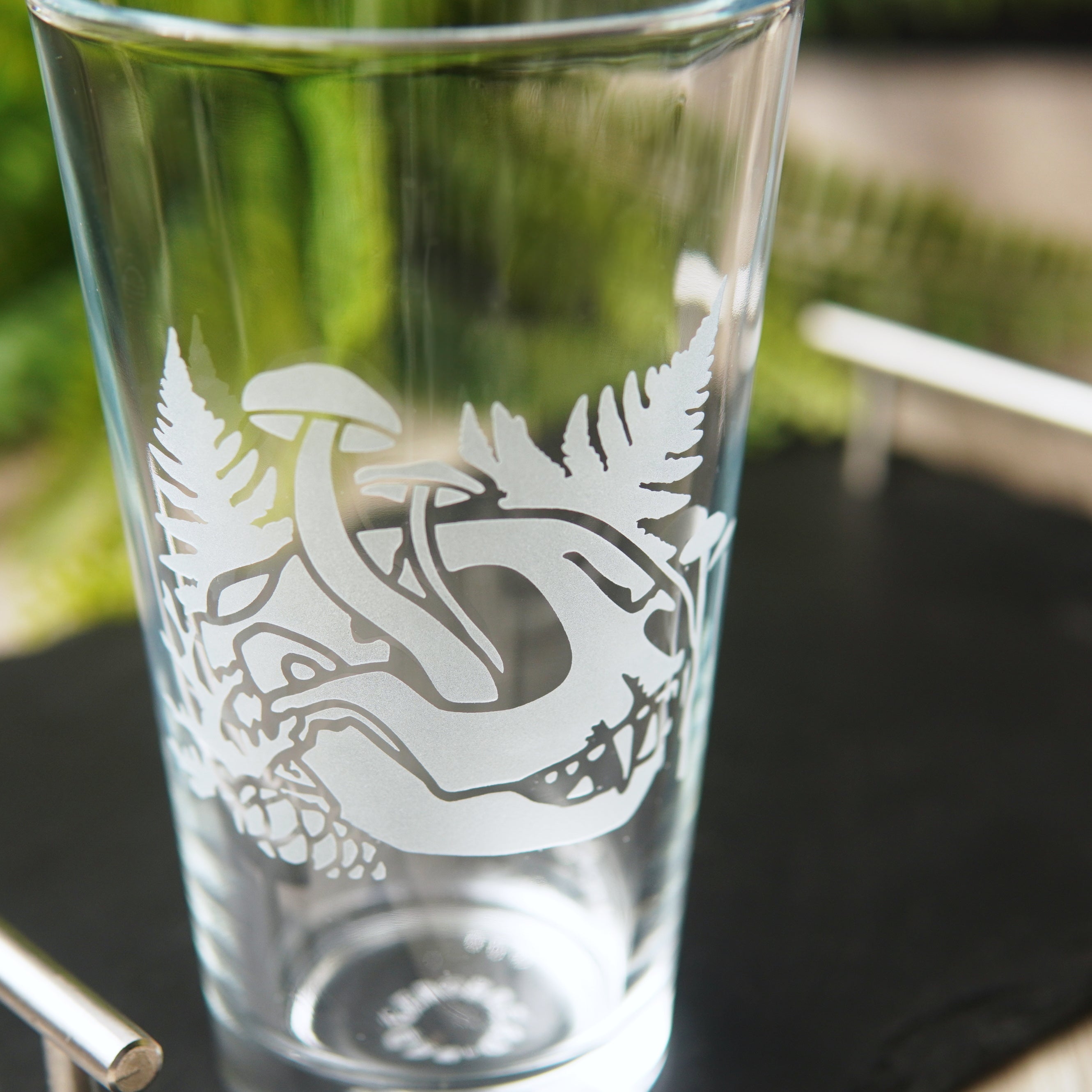 etched pint glass with a cat skull, ferns, and mushrooms