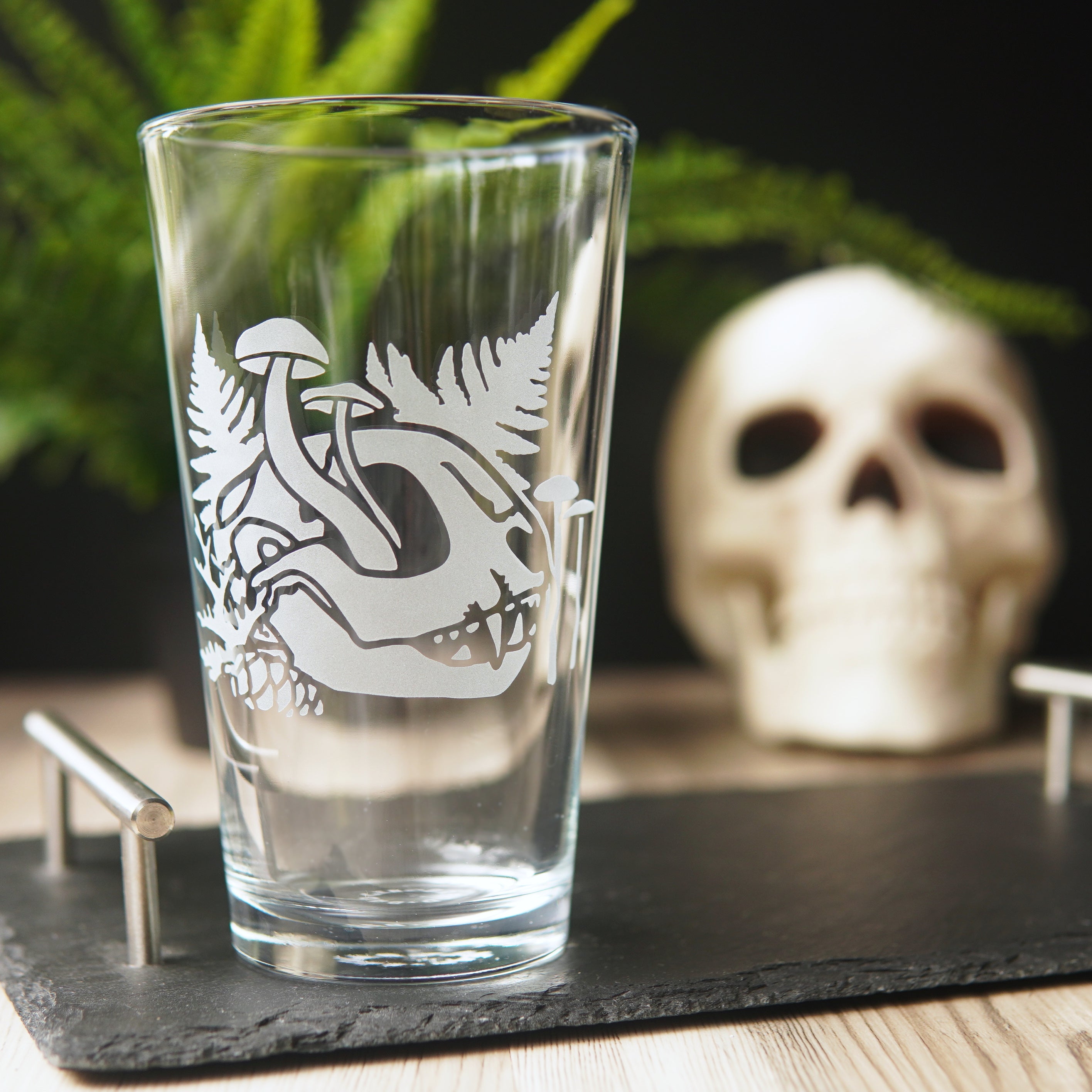 etched pint glass with a cat skull, ferns, and mushrooms