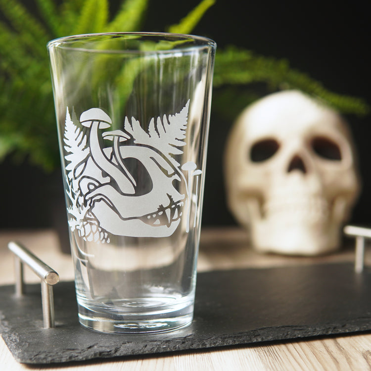 etched pint glass with a cat skull, ferns, and mushrooms