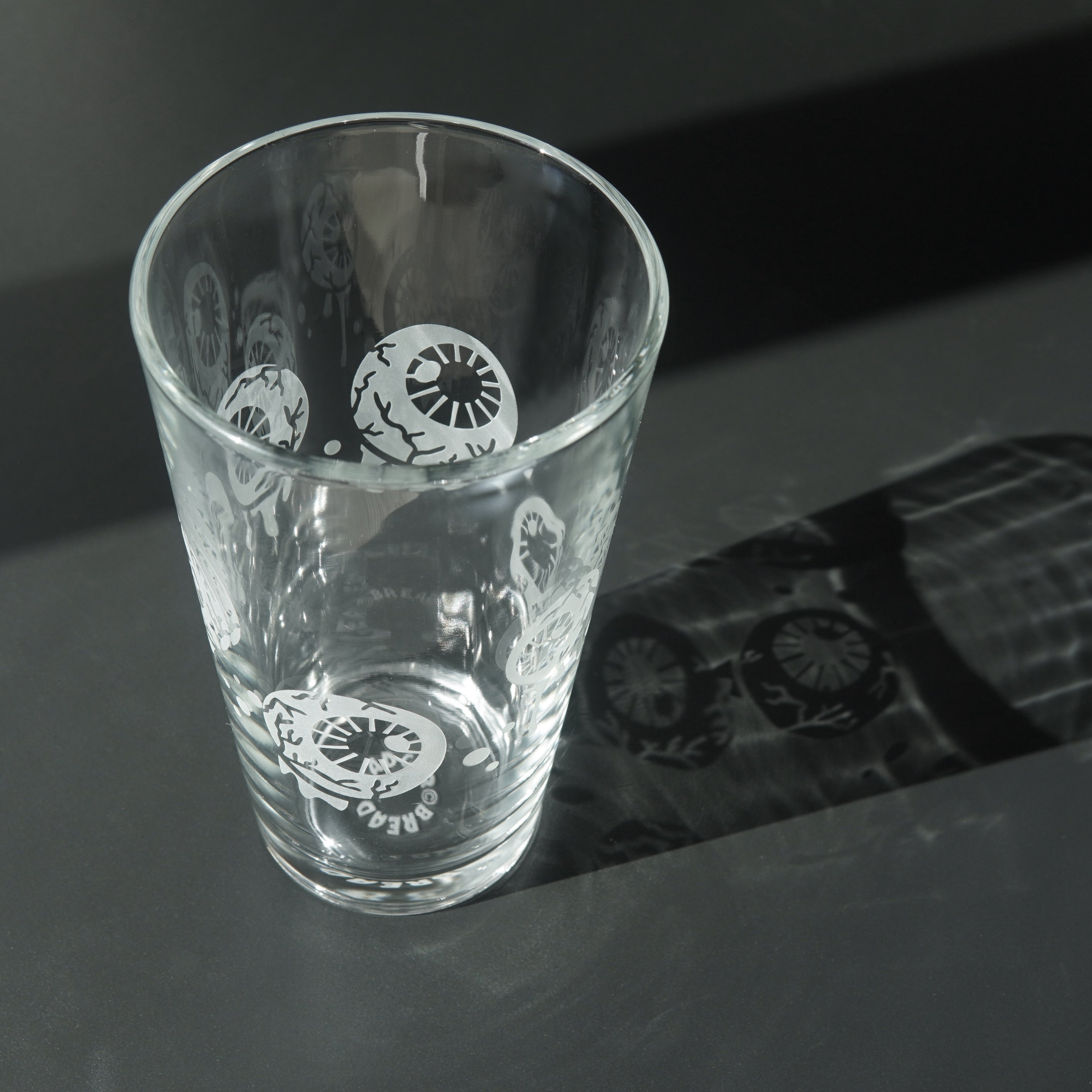 Pint glass engraved with eyeballs. Light is shining through the glass and displaying a shadow next to it showing the etched design.