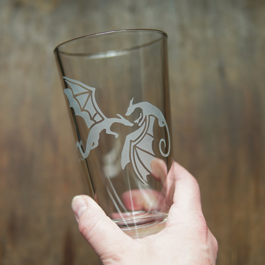 Pint glass engraved with a pair of dragons, held by a hand