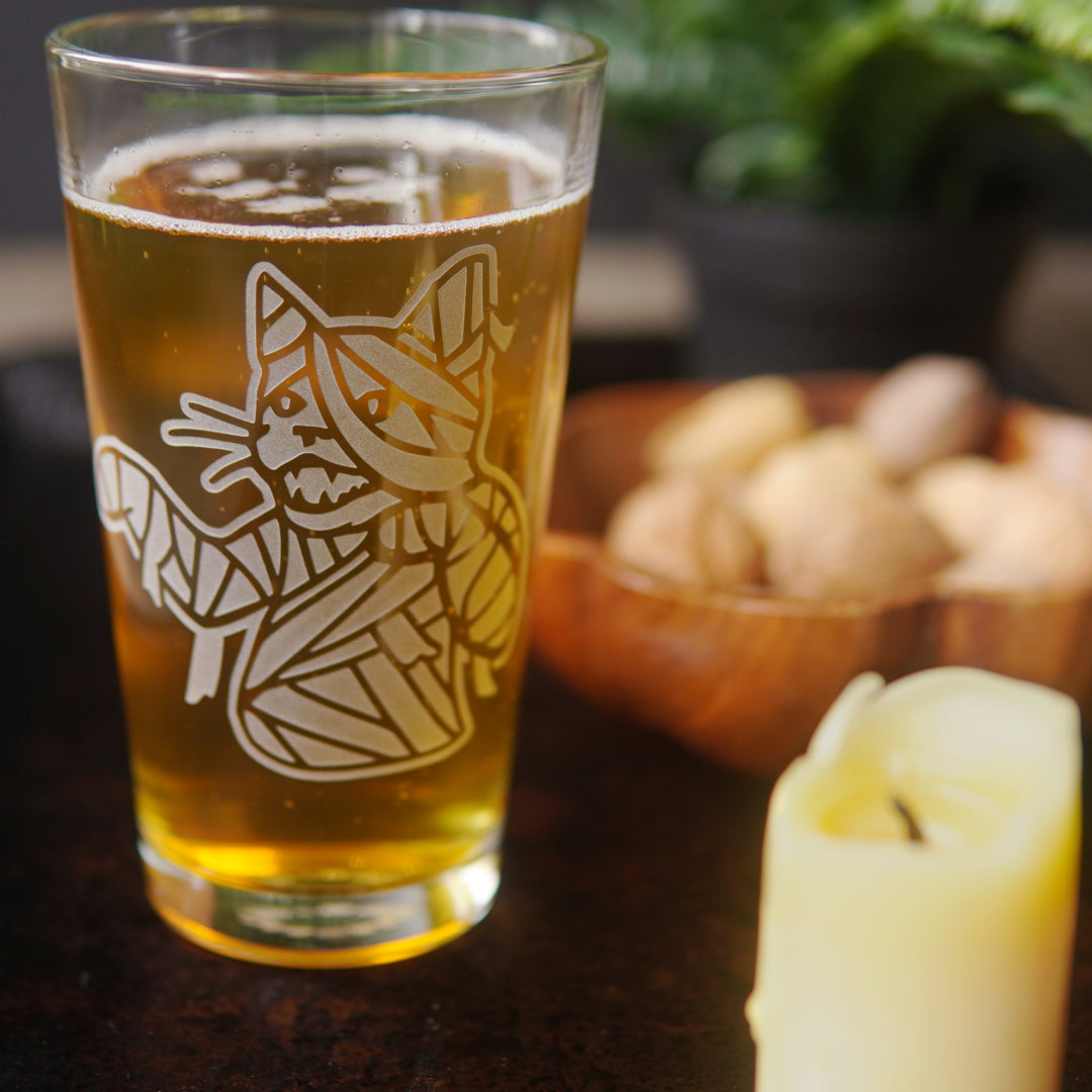 mummy cat pint glass beside a candle and bowl of nuts