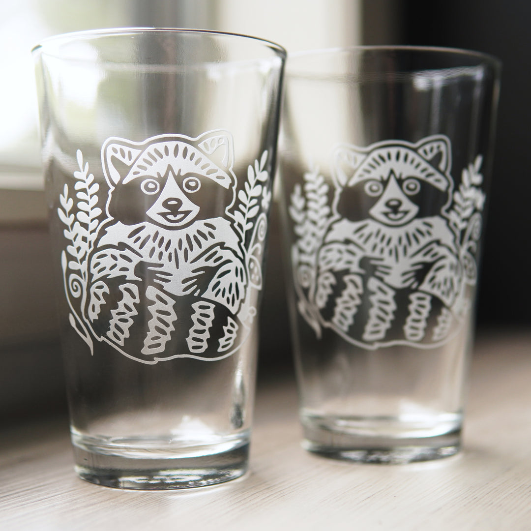 pair of pint glasses engraved with cute, smiling raccoons