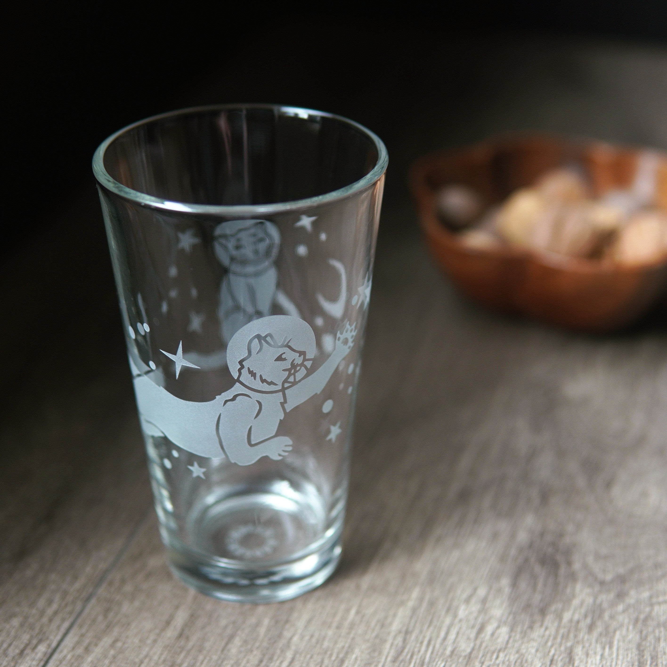 a pint glass engraved with space cats all over it