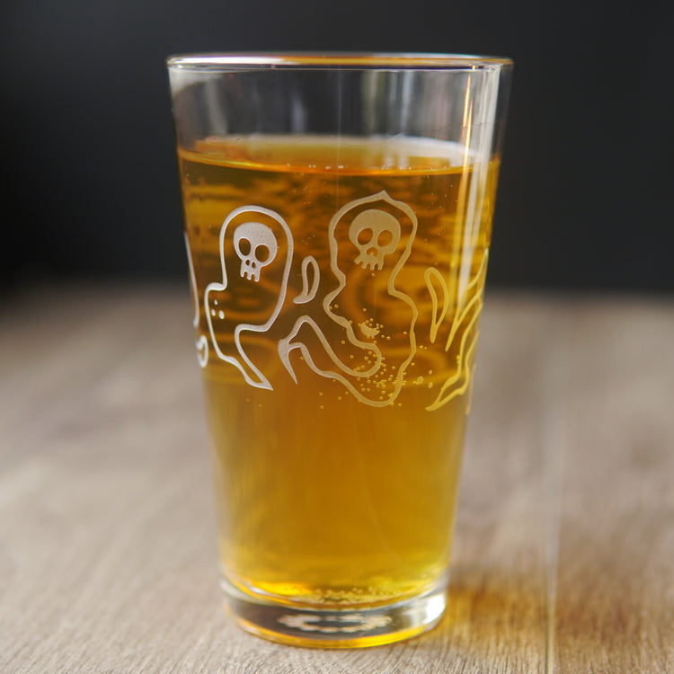 pint glass etched with ghosts with skull faces, full of yellow beer