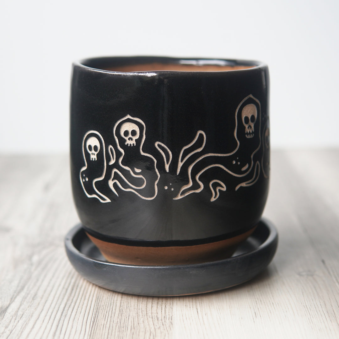 Black ceramic pot with white ghost design on a light background