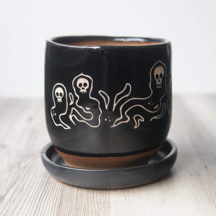 Black ceramic pot with white ghost design on a light background