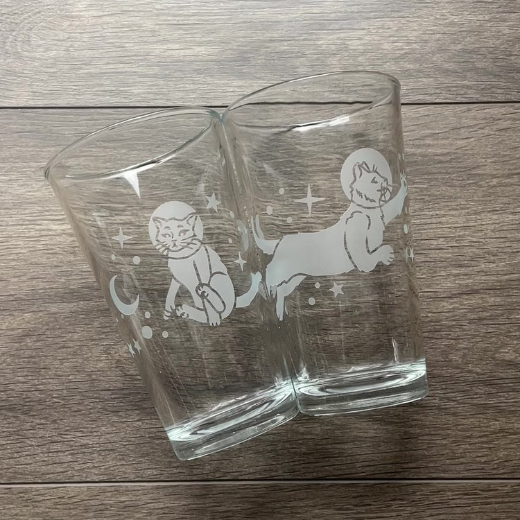 video comparing pint glasses with space cats engraved on them. There is a set of two, one with each cat design, and a third glass with both cat designs wrapping all the way around.