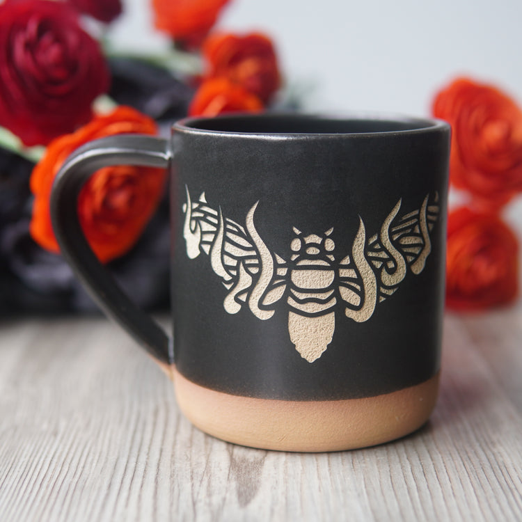 black flaming cicada mug, with red, orange, and black flowers behind it