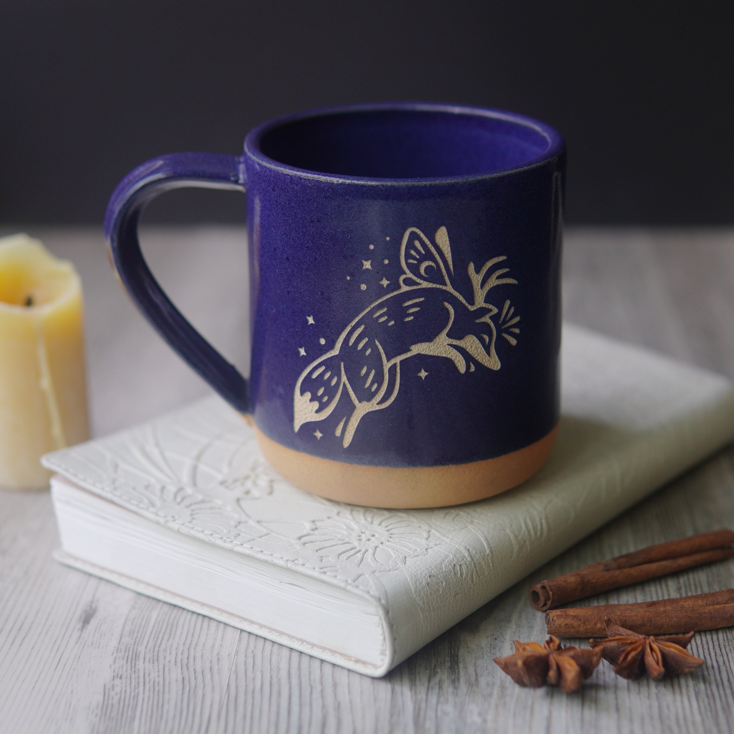 Fox Fairy engraved pottery mug in cobalt blue glaze, with a book and candle