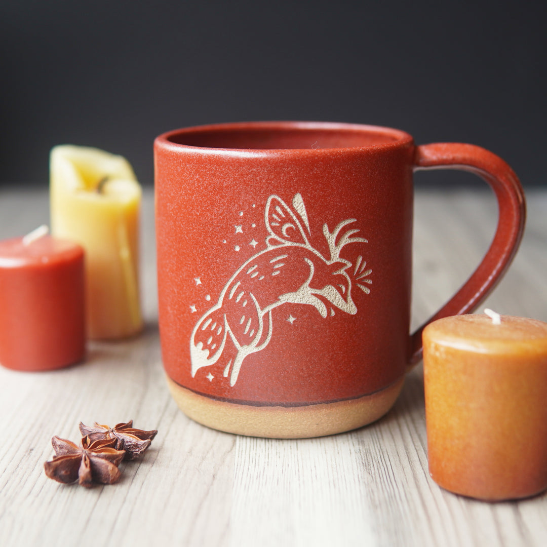 Fox Fairy engraved pottery mug in paprika red glaze, next to candles