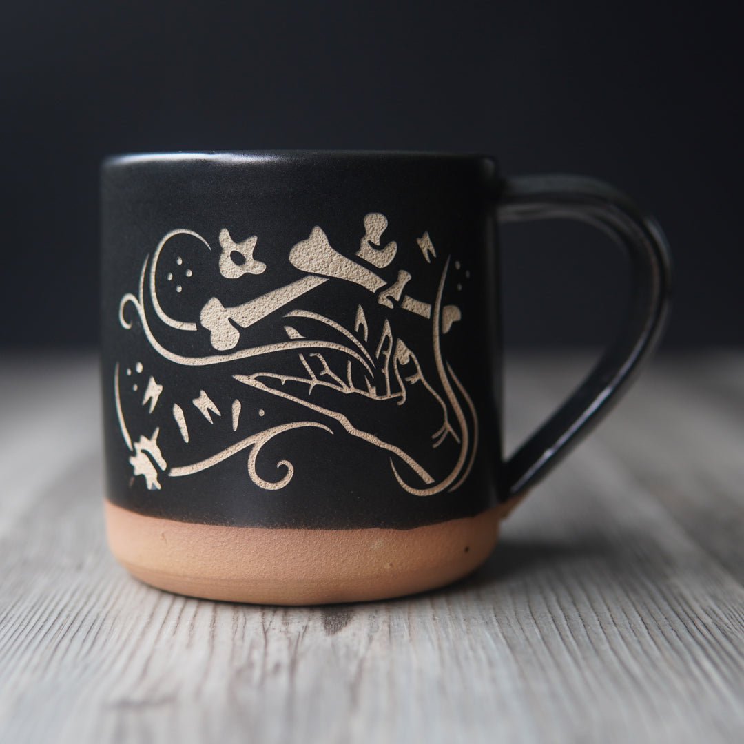 necromancer hand with bones and floating teeth, engraved onto a mug