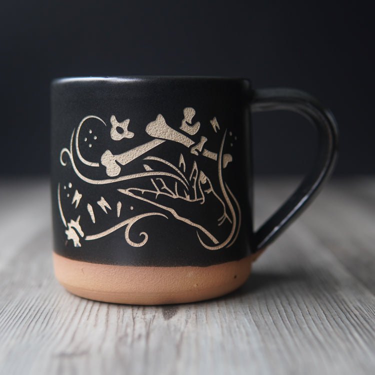 necromancer hand with bones and floating teeth, engraved onto a mug