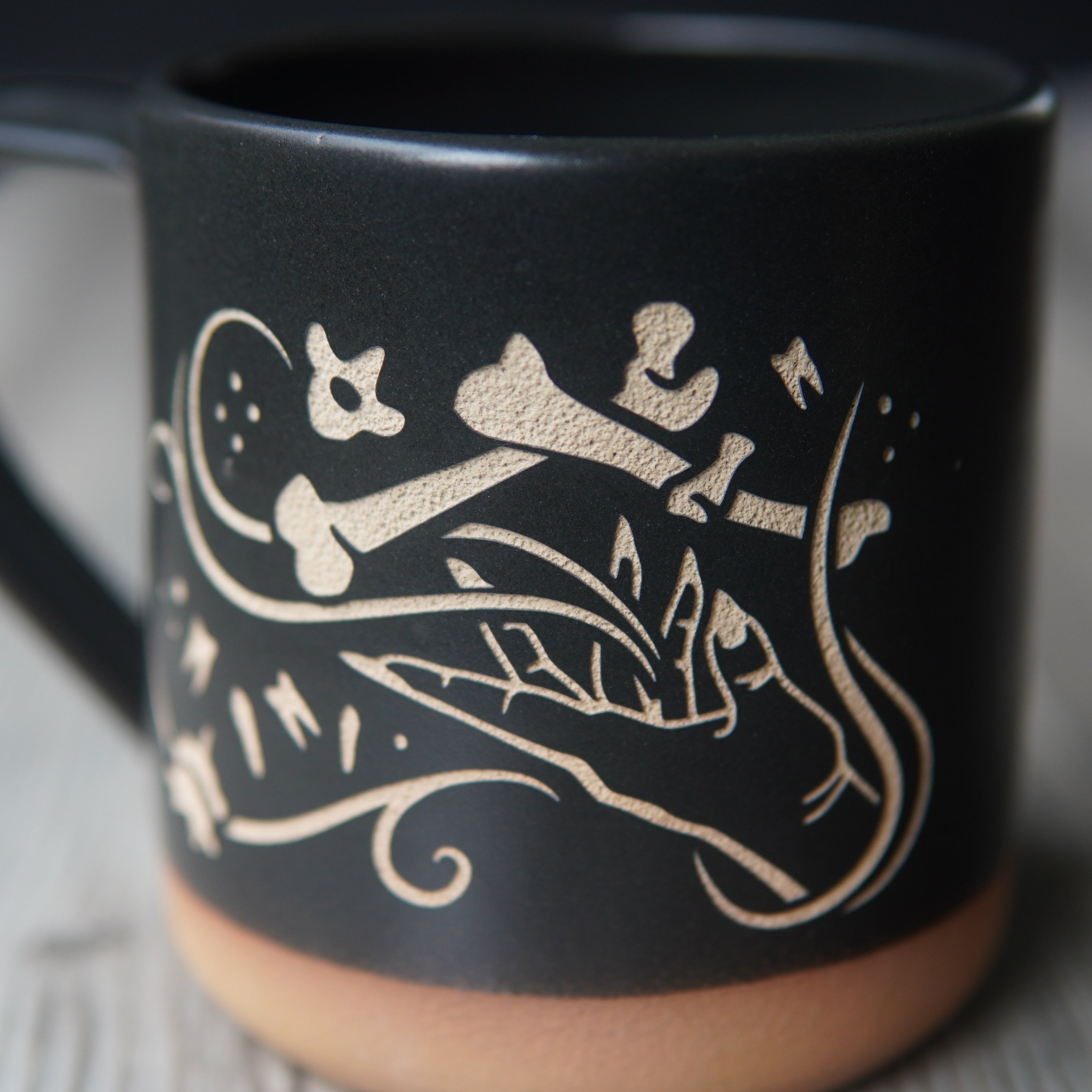 necromancer hand with bones and floating teeth, engraved onto a mug