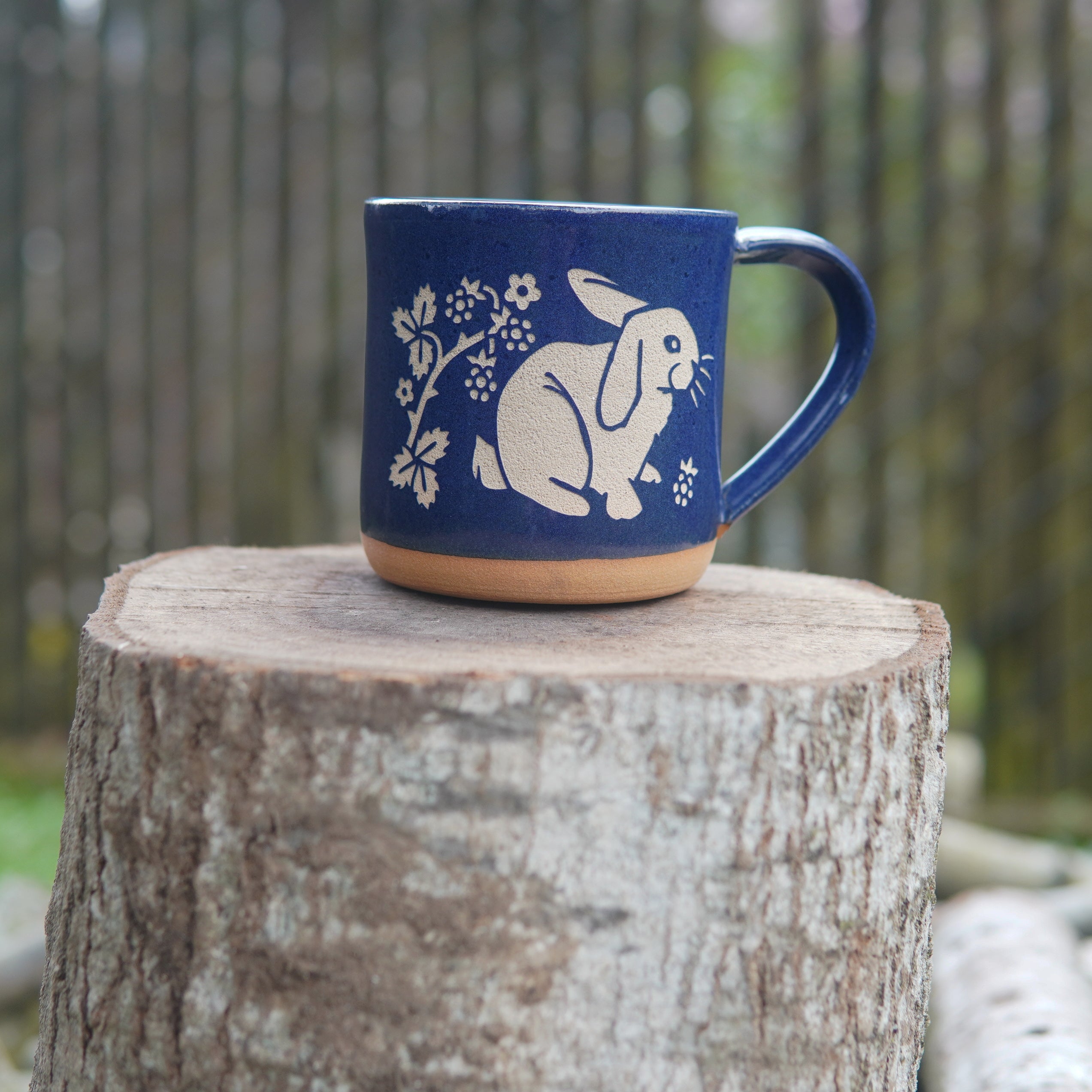 cobalt blue rabbit mug on a stump, in front of a fence