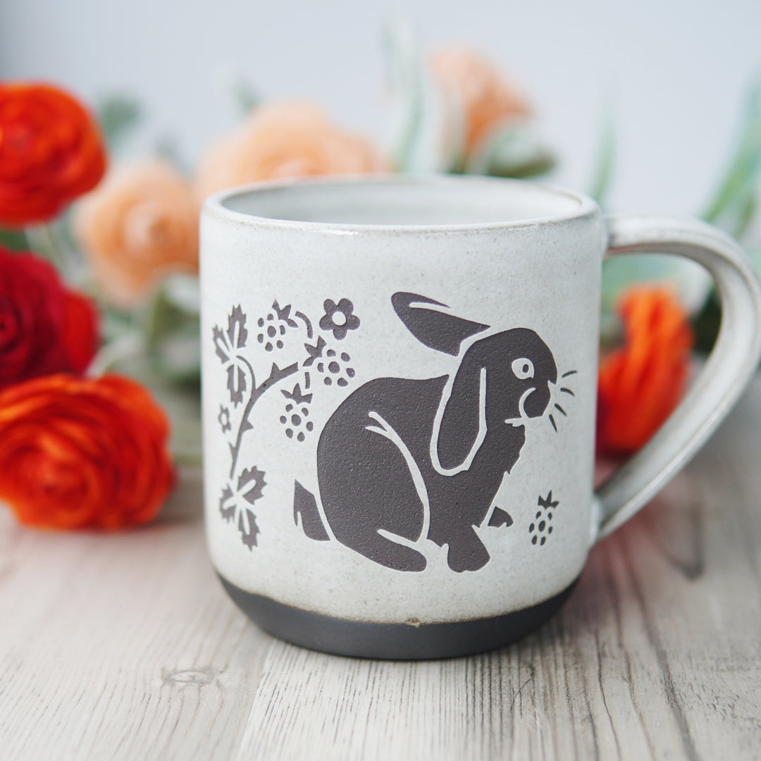 white glazed rabbit mug in dark brown clay, in front of ranunculus flowers