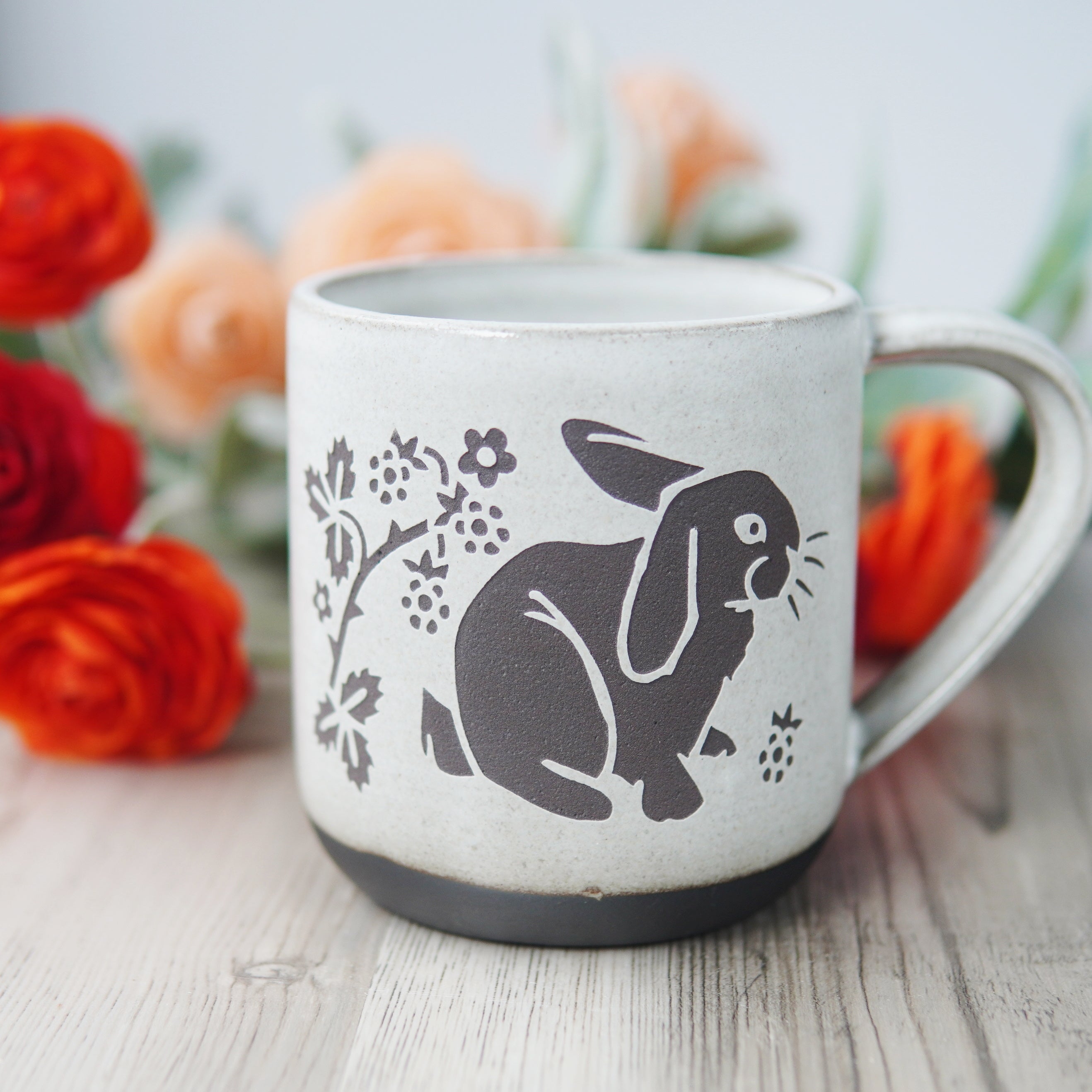 white glazed rabbit mug in dark brown clay, in front of ranunculus flowers