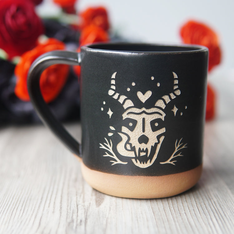 skull with horns and long tongue engraved on a black mug