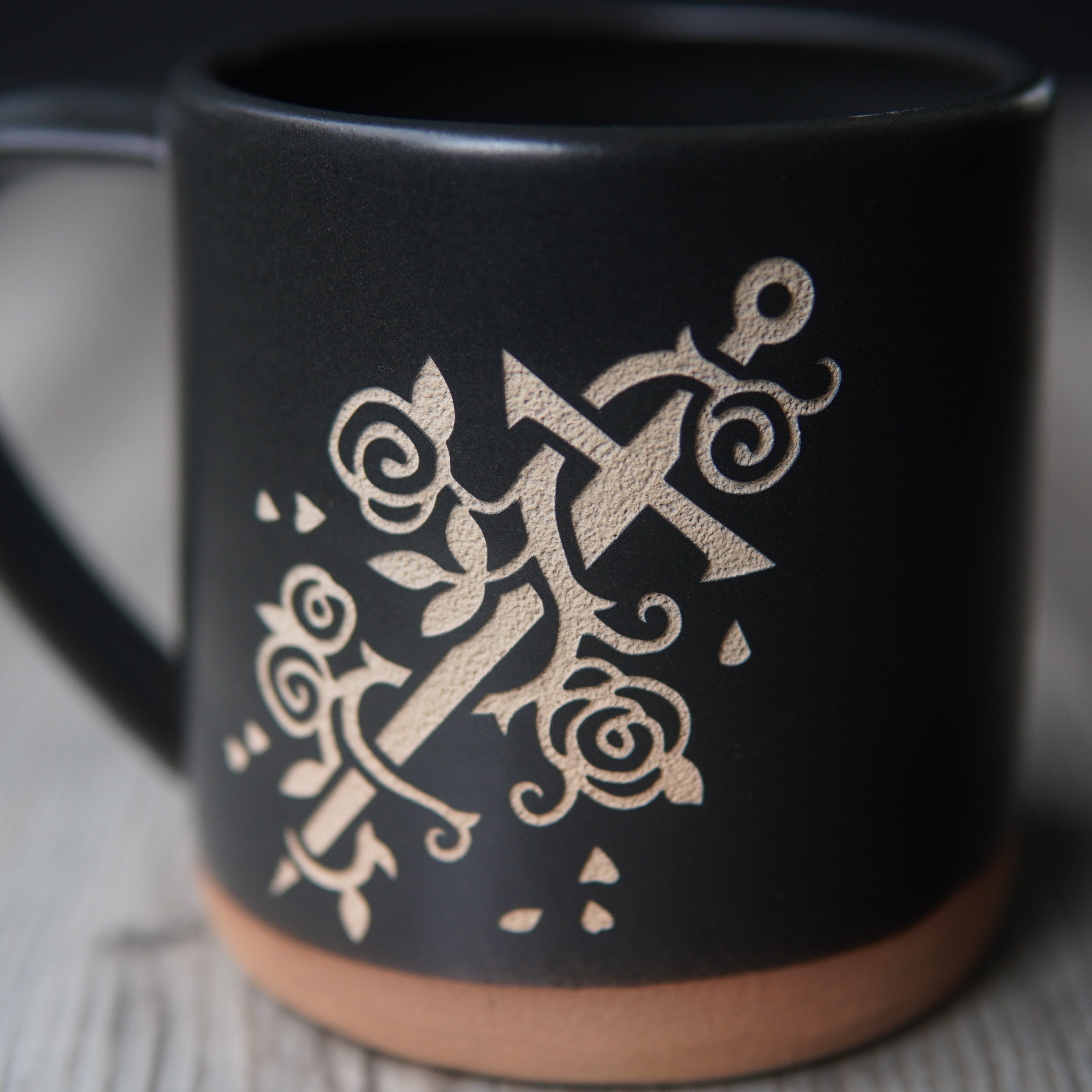 sword wrapped with a vine of roses, engraved on a black mug, close up