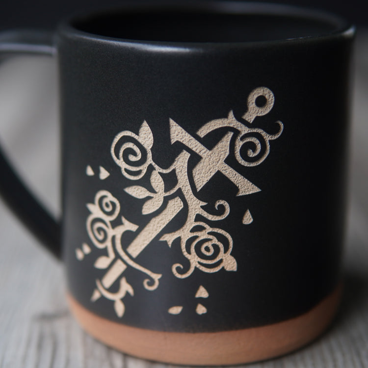 sword wrapped with a vine of roses, engraved on a black mug, close up