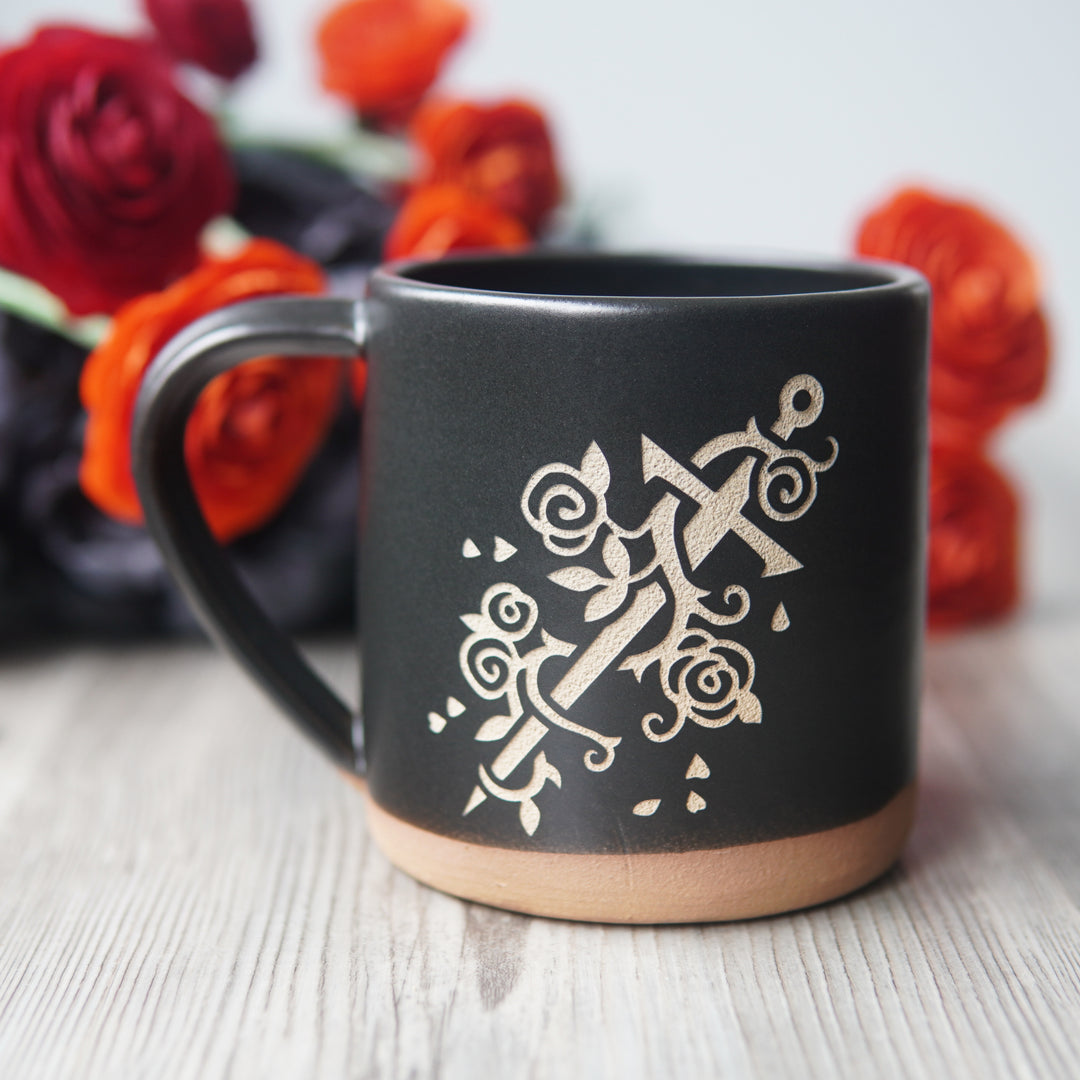sword wrapped with a vine of roses, engraved on a black mug
