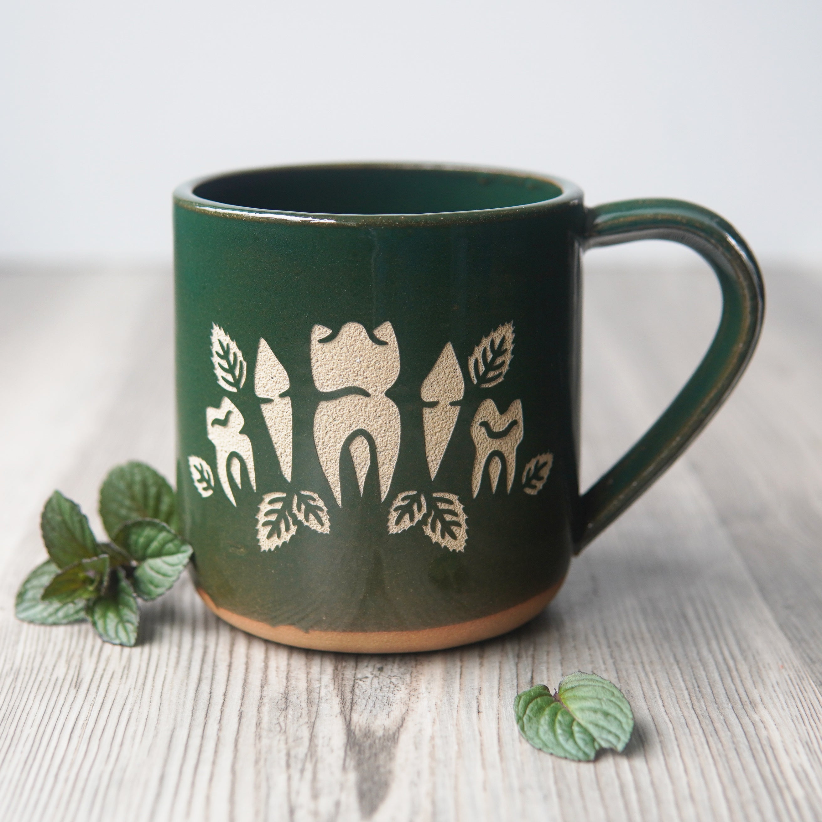 teeth and mint leaves engraved onto a green mug