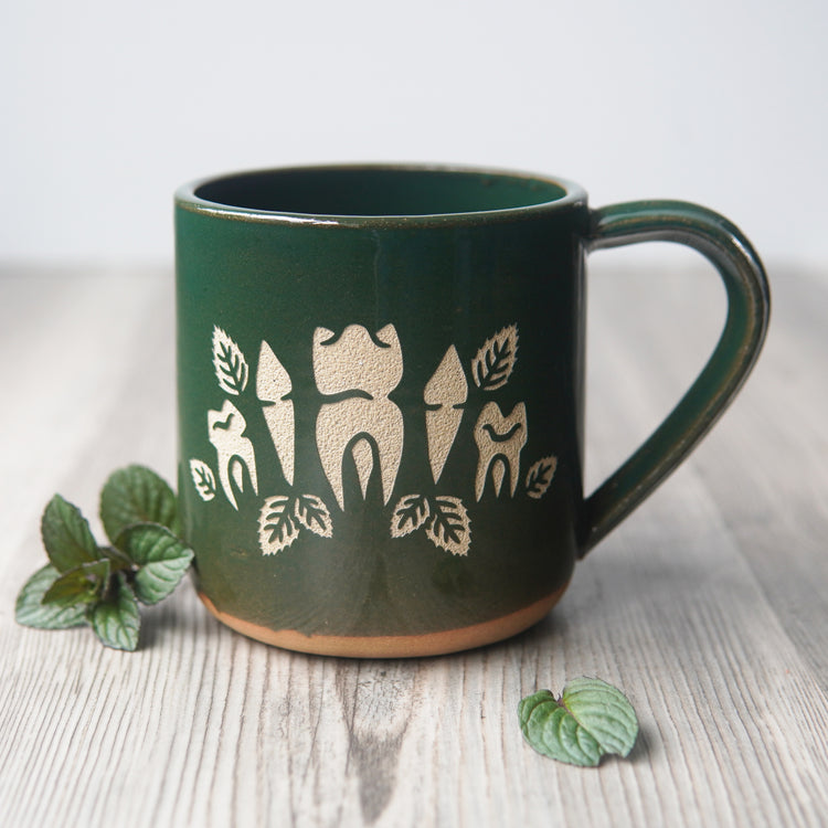 teeth and mint leaves engraved onto a green mug