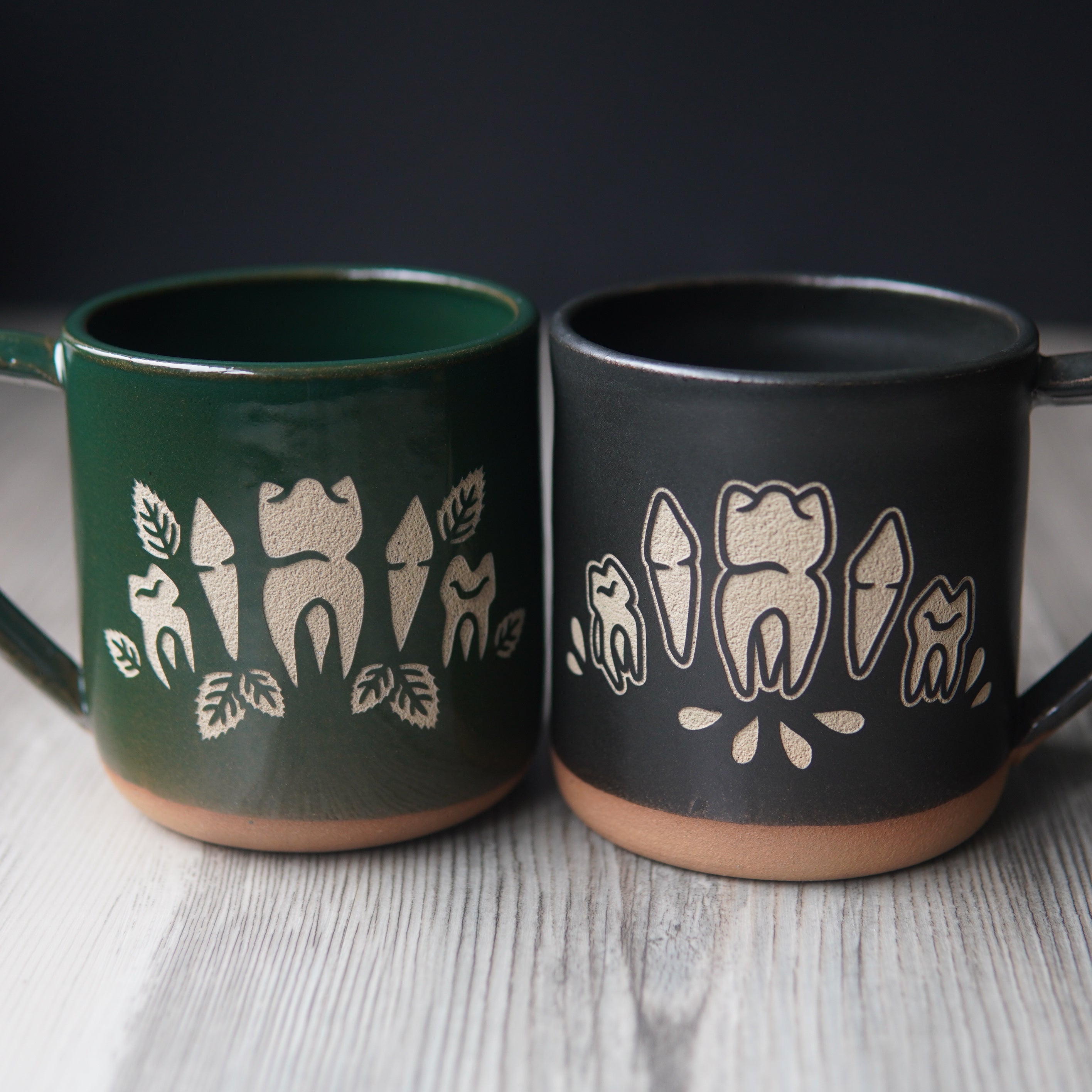 teeth engraved onto green and black pottery mugs