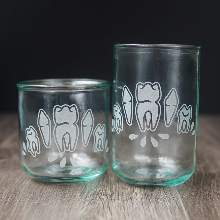 Four teeth with blood droplets engraved onto short and tall drinking glasses. The glass has a slight bluegreen tinge.