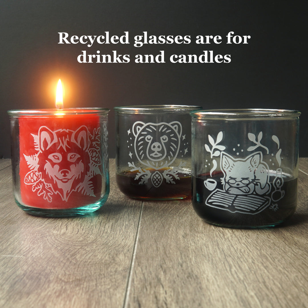 text reads: "recycled glasses are for drinks and candles" above three short etched tumblers. One has a lit candle inside it, the others have dark liquids inside.