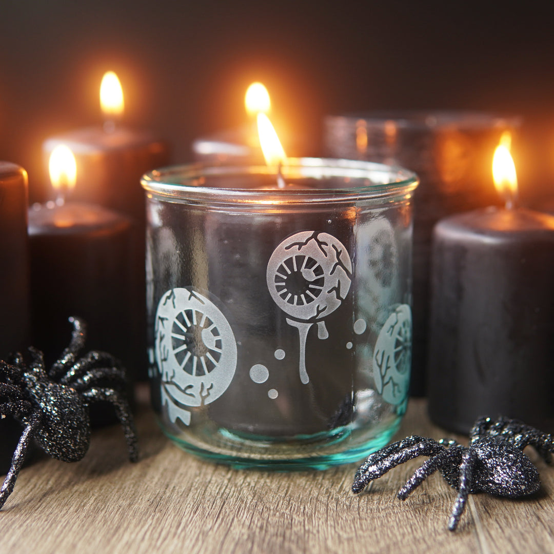 eyeballs short glass cup holding a black candle, surrounded by more lit candles and glittery spiders