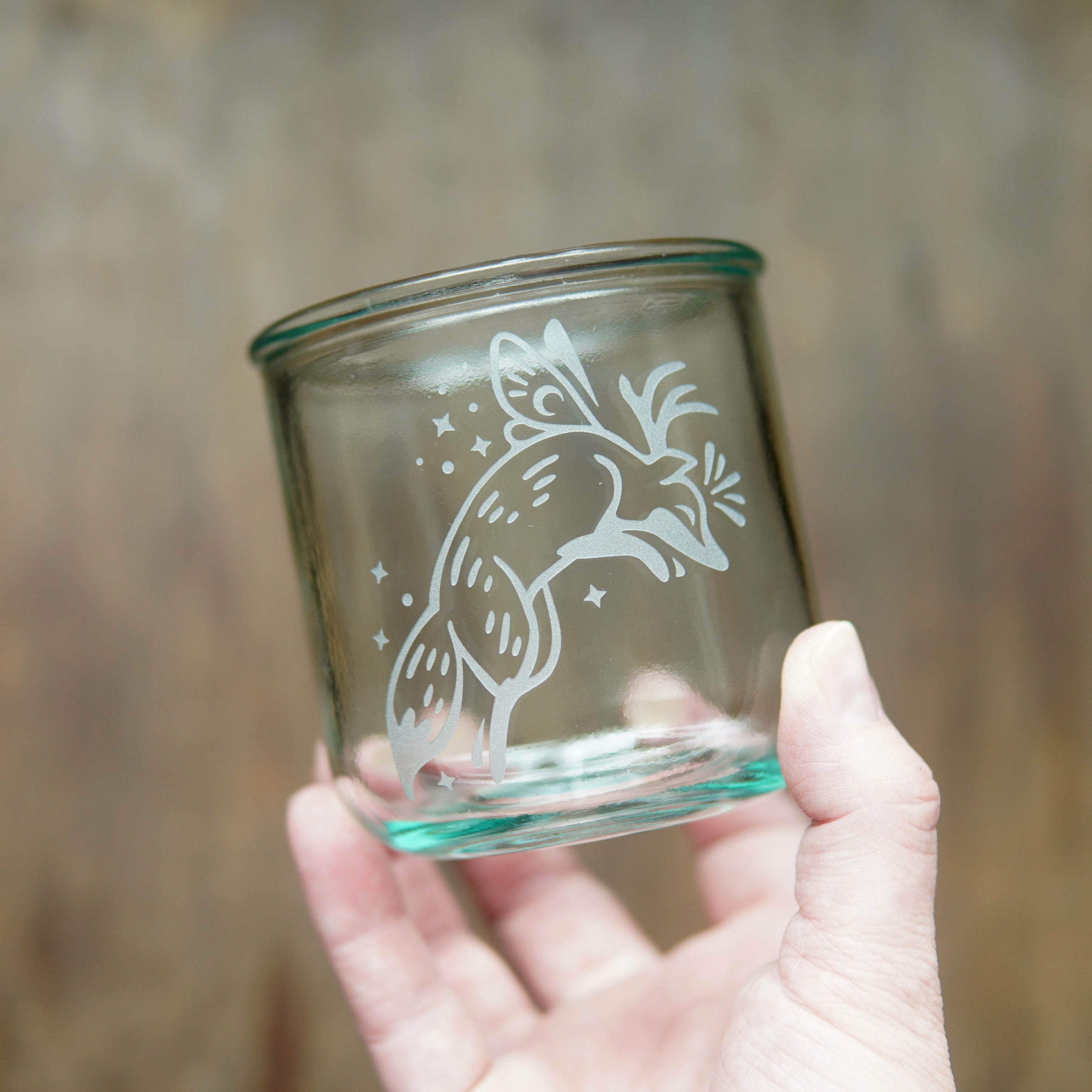 Fox with fairy wings etched onto a short glass, held by a hand