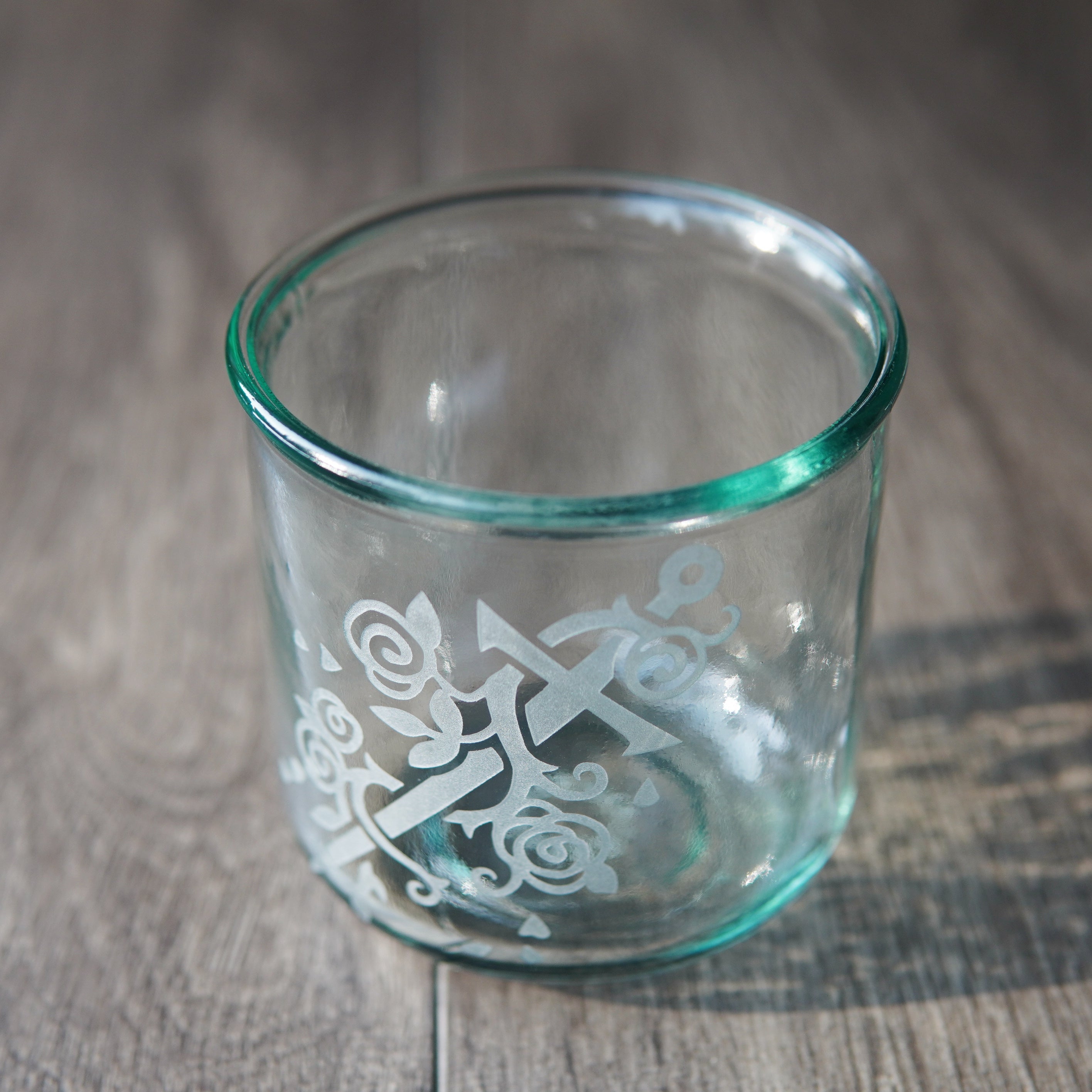 Sword wrapped with a rose vine engraved onto a tall drinking glass. The glass has a slight bluegreen tinge and is viewed from slightly above.