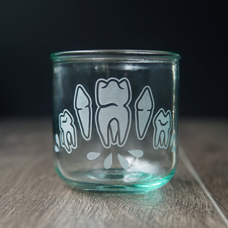 Four teeth with blood droplets engraved onto a short drinking glass. The glass has a slight bluegreen tinge.