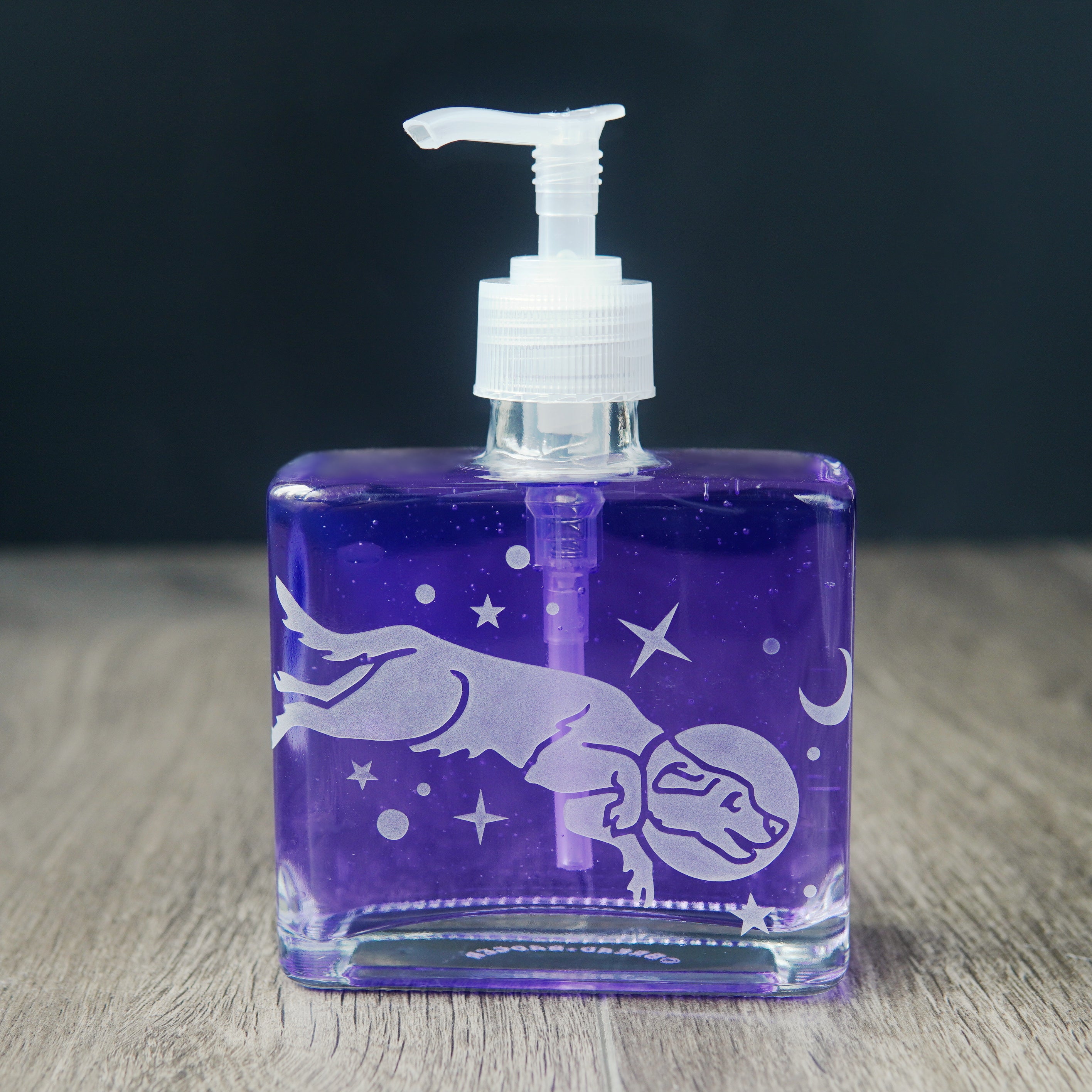 a square glass space dog soap dispenser filled with purple dish soap
